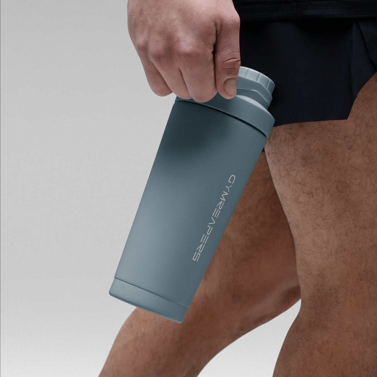 Athlete holding the Lake Blue stainless steel shaker bottle by the built in carry loop handle with the wordmark logo facing outward