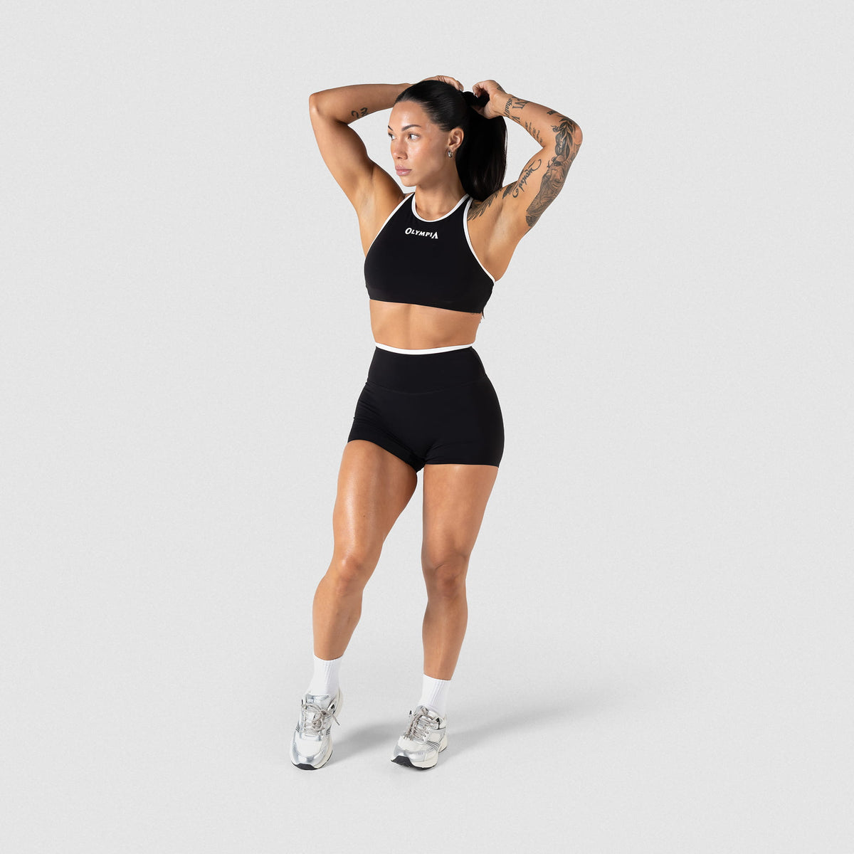 Full body view of female model wearing the black and white contrasting 4" Olympia training shorts, paired with a matching bra