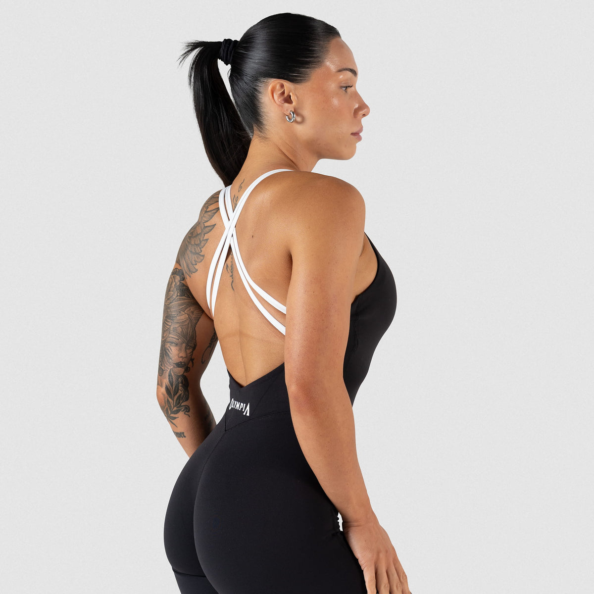 Side view of model wearing the Olympia Bodysuit in black that shows the V back in black and white contrast criss cross straps