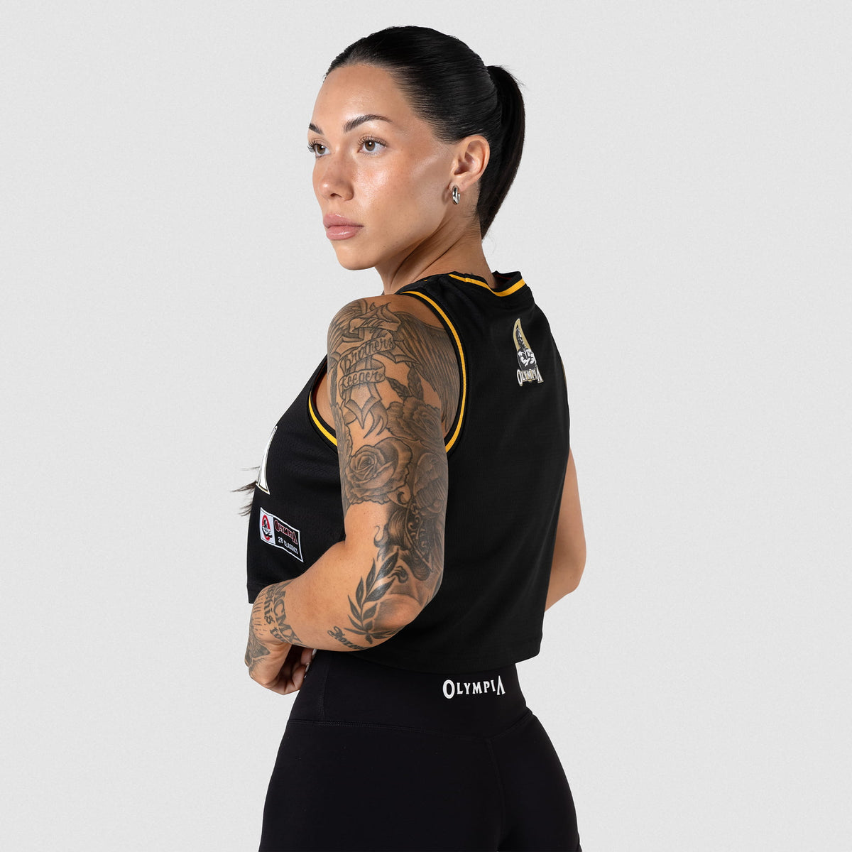 Champions Gold Crop Jersey | Female model angled away to show the side angle and back view of the cropped black jersey
