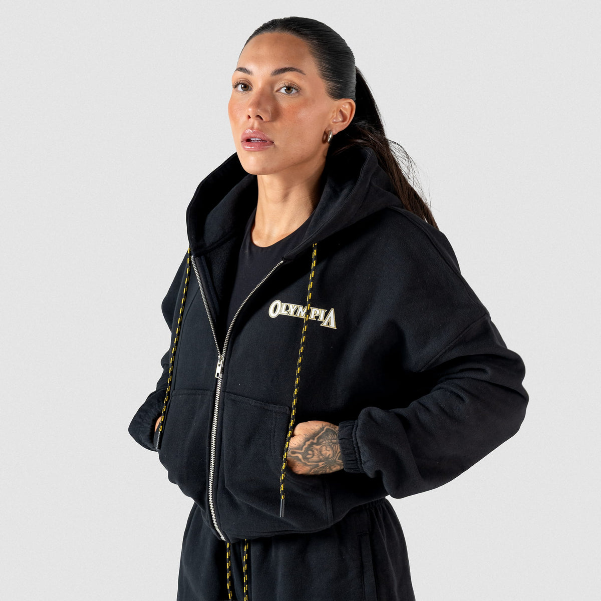 Champions Gold Cropped Zip-Up Hoodie | Front View, on model of half zipped hoodie, gold and black adjustable drawstrings, and "Olympia" wordmark logo