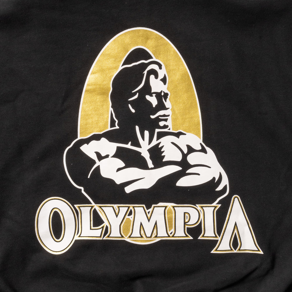 Champions Gold Cropped Zip-Up Hoodie | Close up of gold, white, and black "Olympia" Champions Gold event logo