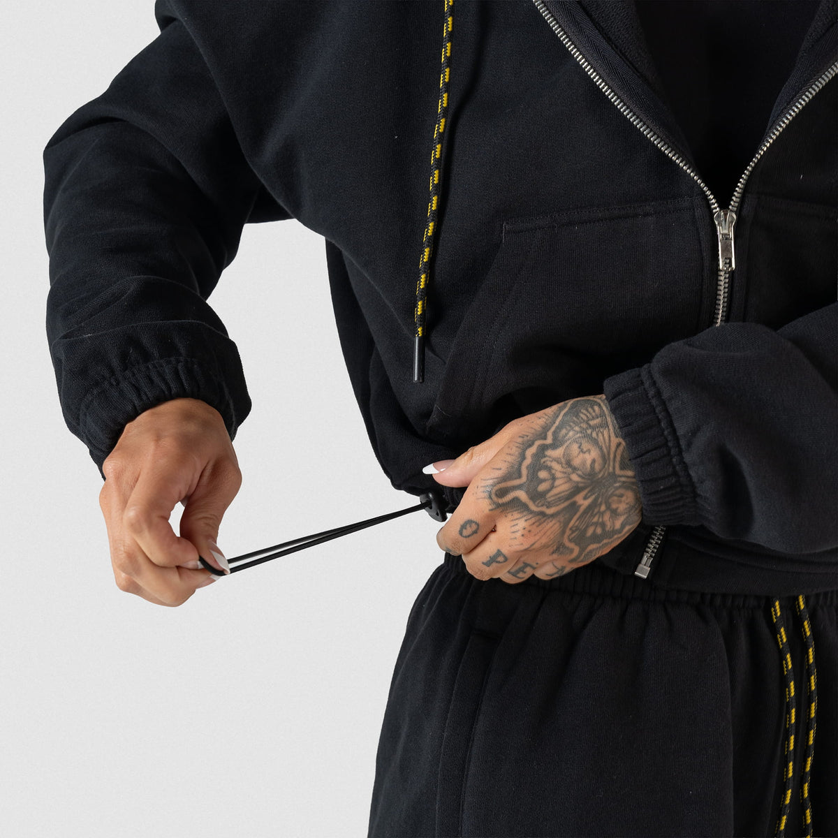 Champions Gold Cropped Zip-Up Hoodie | Model adjusting the crop of the hoodie with the adjustable drawstring on the bottom hem