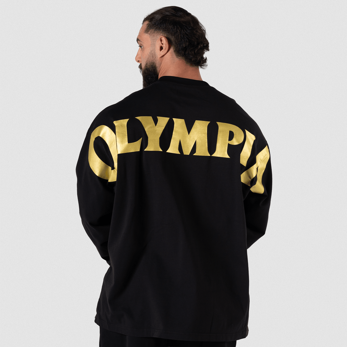 Man wearing black long-sleeve top with gold "OLYMPIA" arched lettering across the back