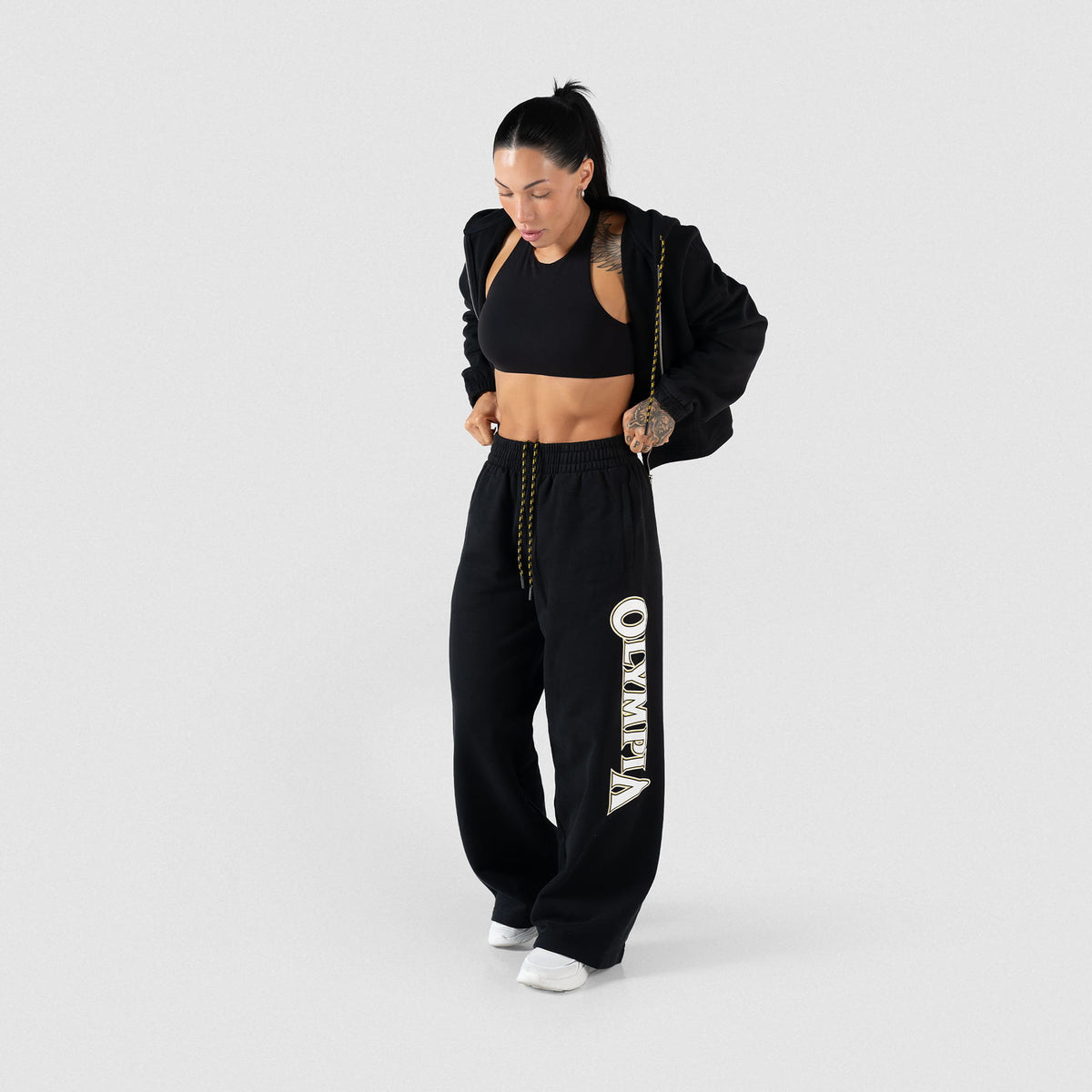 Full body model view of the Champions Gold Wide-Leg Jogger in black, paired with a black bra and black full zip jacket