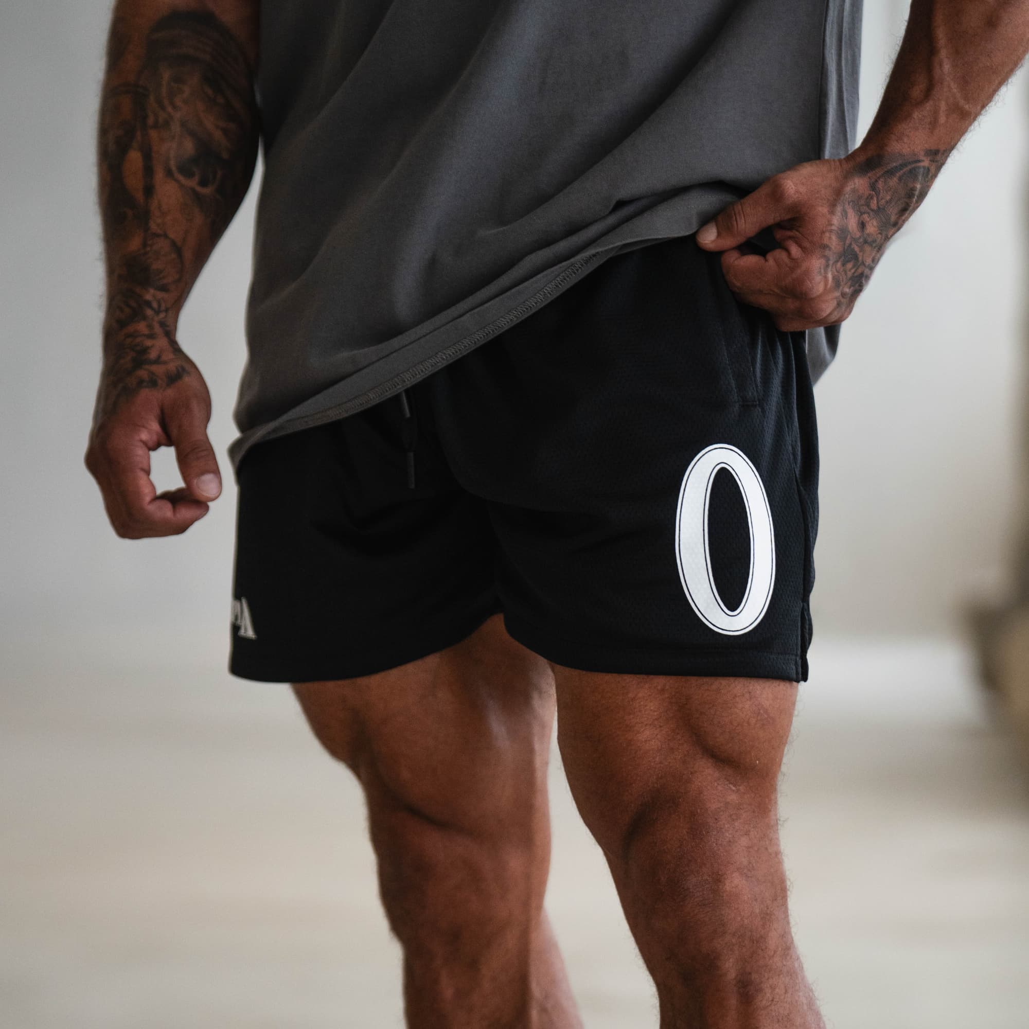 Model wearing Olympia O Mesh Shorts showing large white O graphic printed on the left thigh