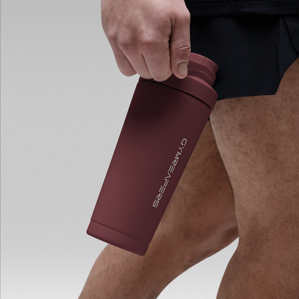 Athlete holding the Burgundy red stainless steel shaker bottle by the built in carry loop handle with the wordmark logo facing outward