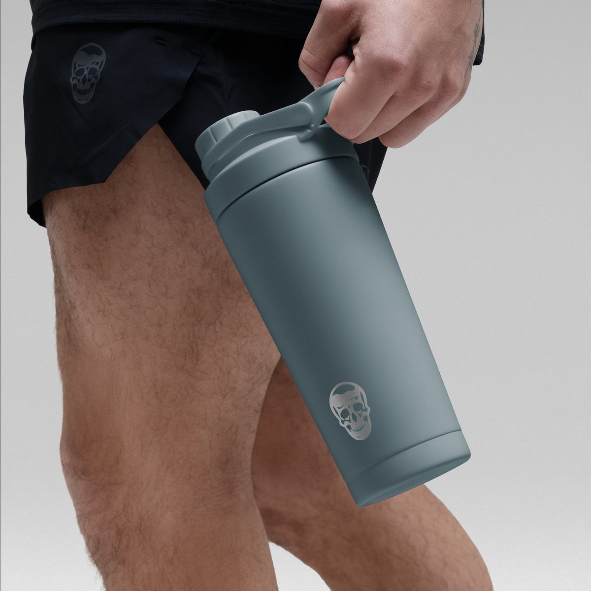 Athlete holding the Lake Blue stainless steel shaker bottle by the built in carry loop handle with the skull logo facing outward
