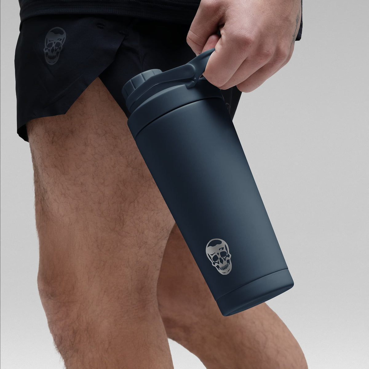 Athlete holding the Navy blue stainless steel shaker bottle by the built in carry loop handle with the skull logo facing outward