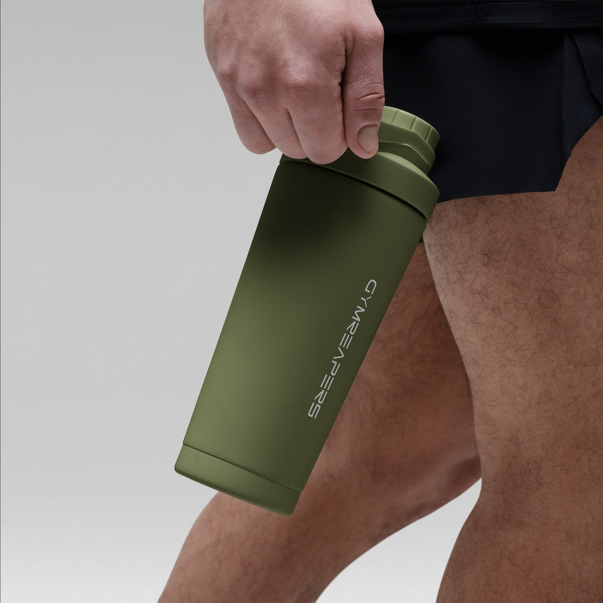 Athlete holding the OD Green stainless steel shaker bottle by the built in carry loop handle with the wordmark logo facing outward