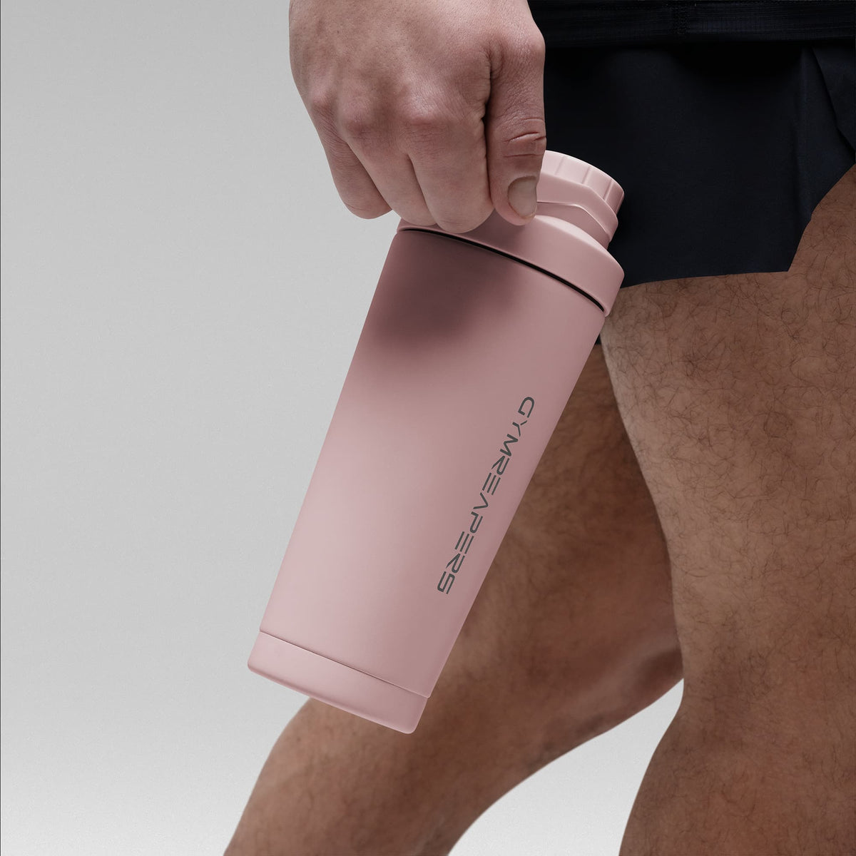 Athlete holding the Light pink stainless steel shaker bottle by the built in carry loop handle with the wordmark logo facing outward
