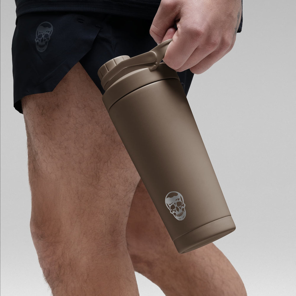 Athlete holding the Toffee Brown stainless steel shaker bottle by the built in carry loop handle with the skull logo facing outward