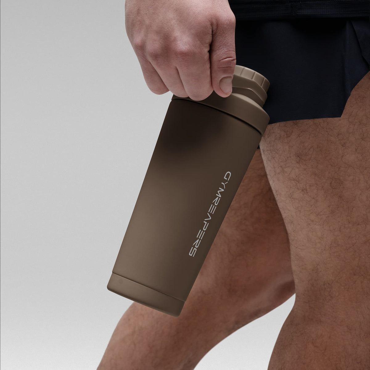 Athlete holding the Toffee Brown stainless steel shaker bottle by the built in carry loop handle with the wordmark logo facing outward