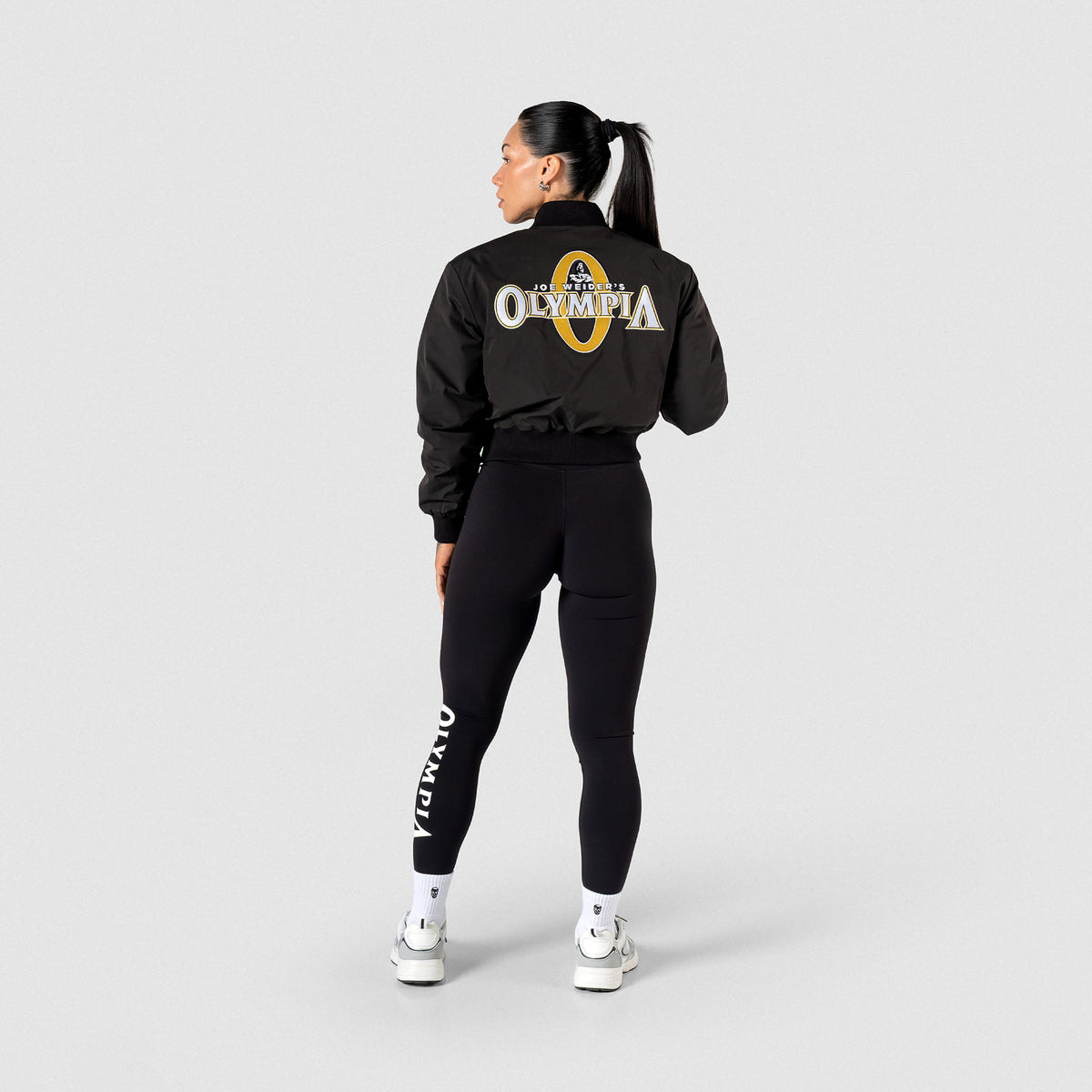 Champions Gold Crop Bomber Jacket | Full Back view of Model wearing the Champions Gold Crop Bomber Jacket with matching women's Olympia leggings