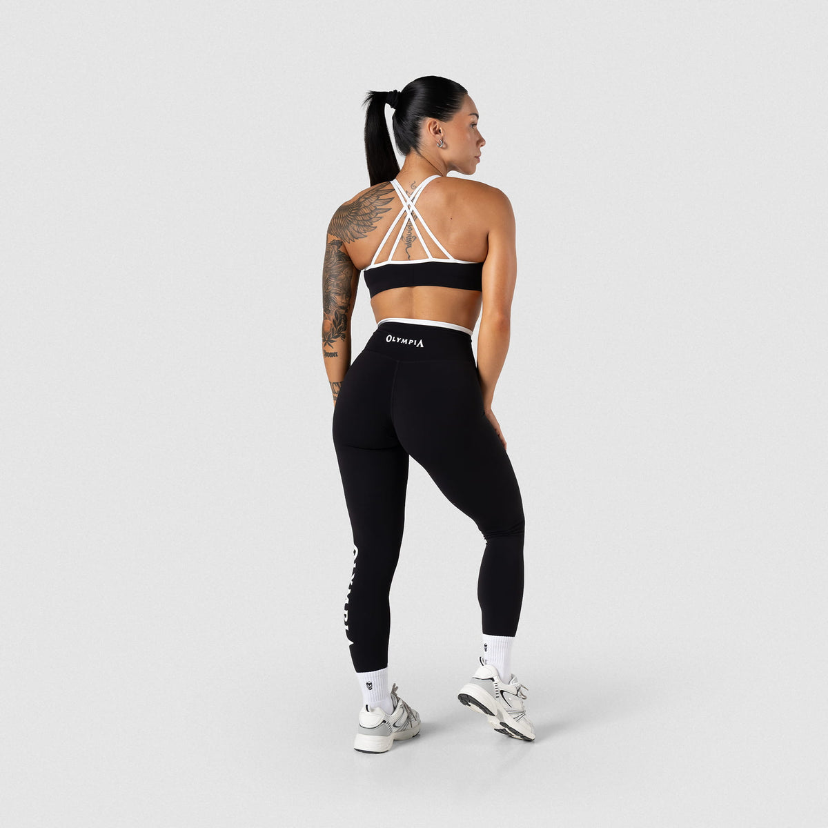 Back view of female model wearing the Olympia black/white contrast high neck sports bra paired with black/white contrast leggings