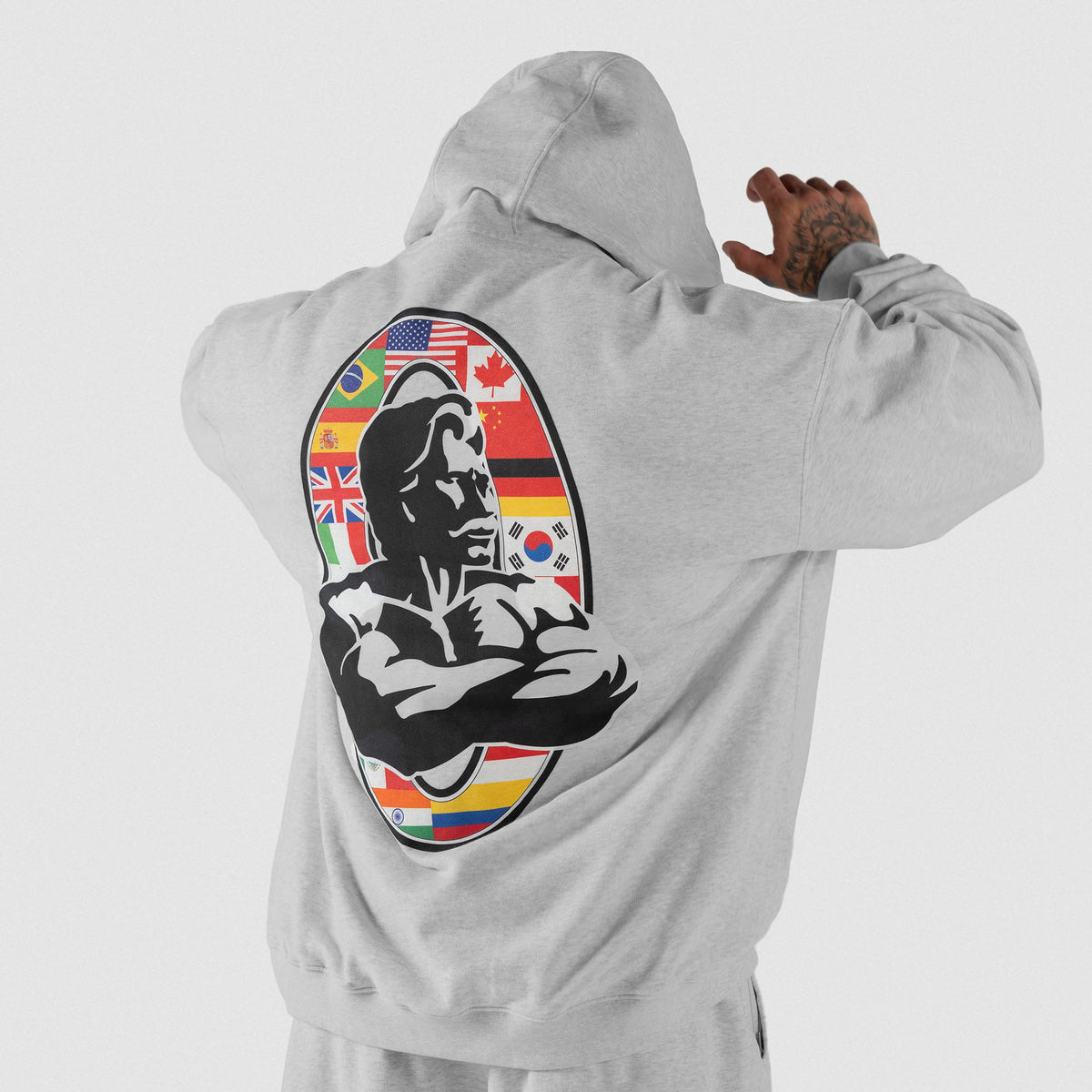 International Division Hoodie | Male model, back view, wearing the gray hoodie with hoodie pulled up, showcasing the large International Division Olympia logo on the back
