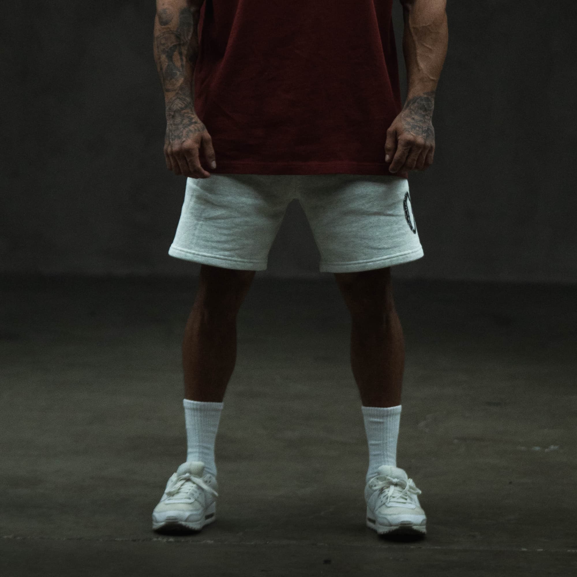 Lifestyle full-body front view of the Olympia Sweat Short styled with white sneakers and socks, showing the relaxed fit and graphic details.