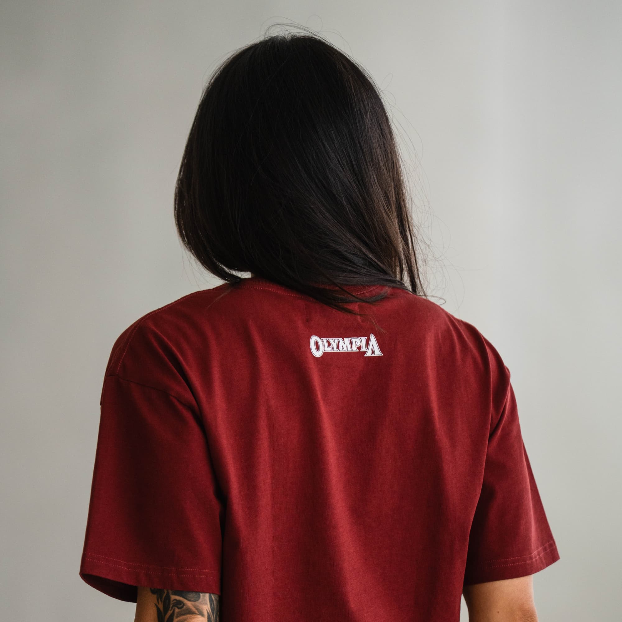 Back view of model wearing the Olympia Cropped Tee in red with small Olympia logo below collar