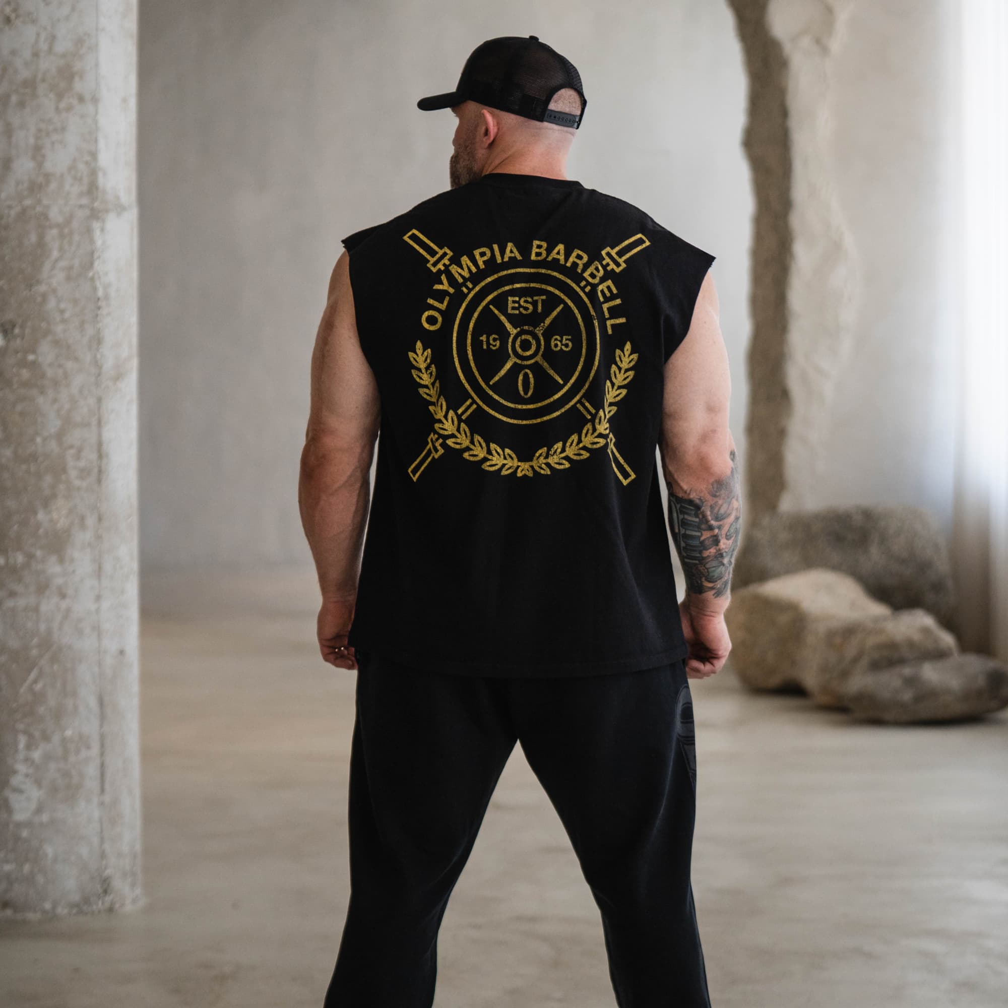 Model wearing the black Olympia Crest Cut Off shown from the back with large gold crest graphic