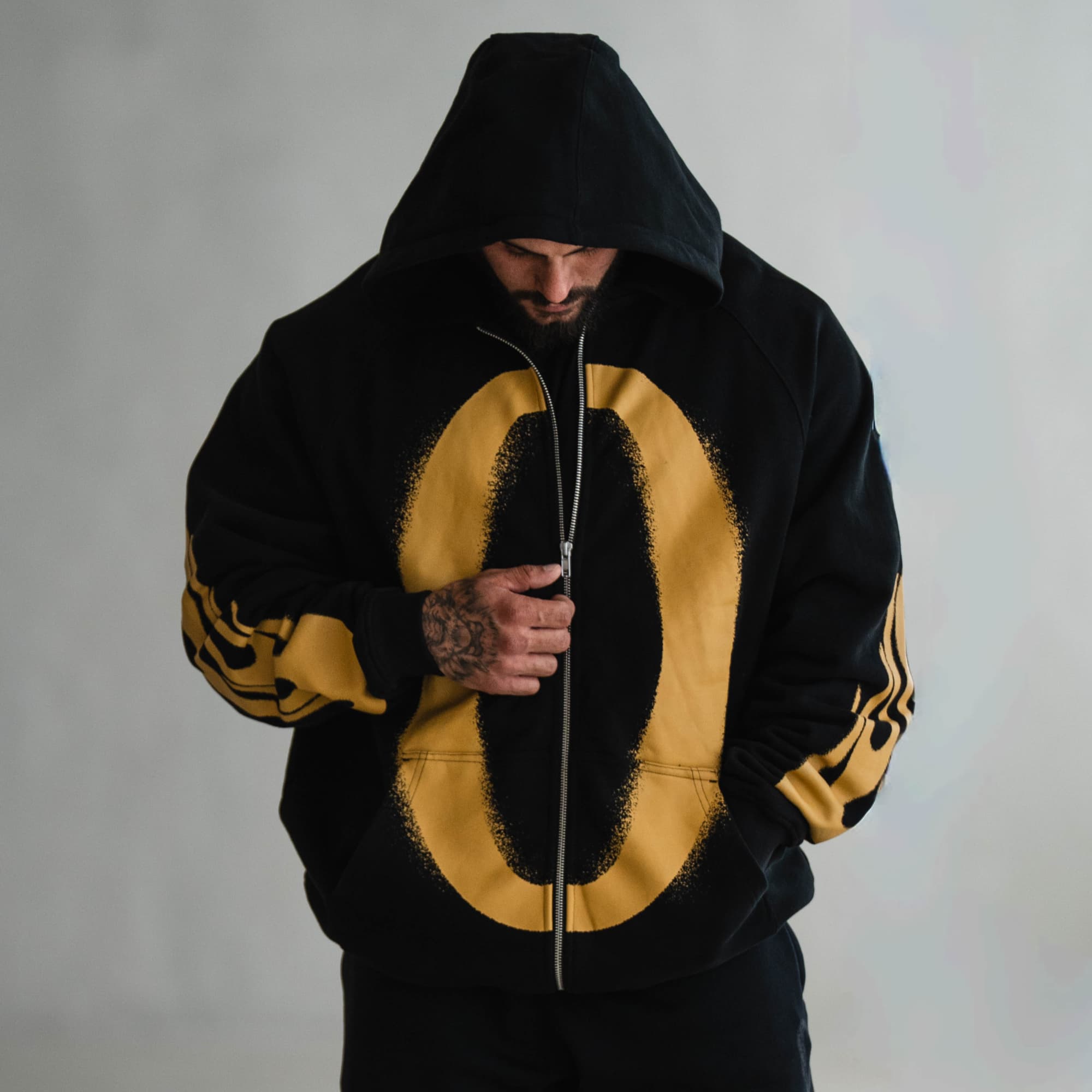 Model wearing the Ring of Fire Zip-Up Hoodie with hood up, looking down while adjusting zipper