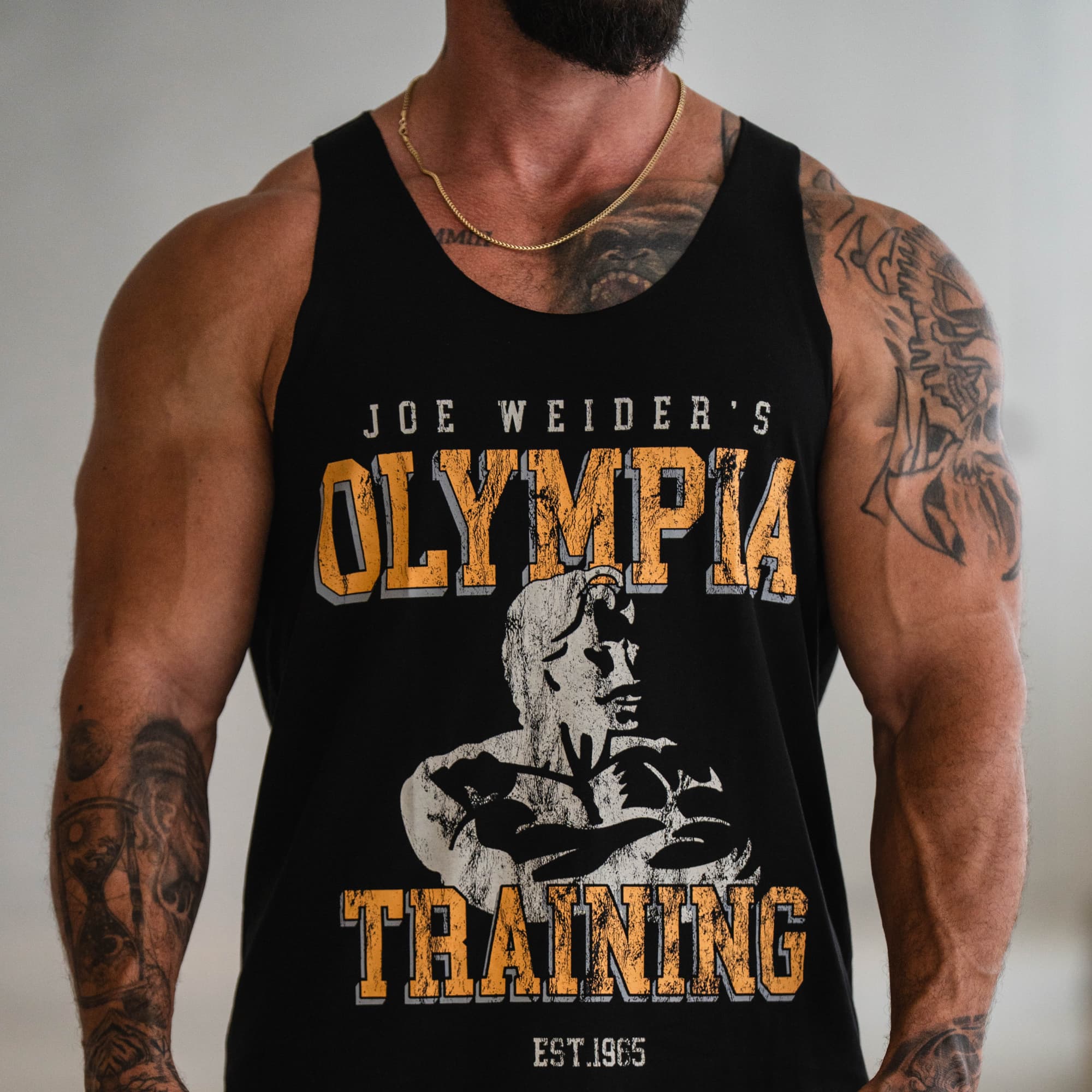 Close-up of the Raw Hem Olympia Training Stringer front graphic with bold Olympia Training text and illustrated physique detail.