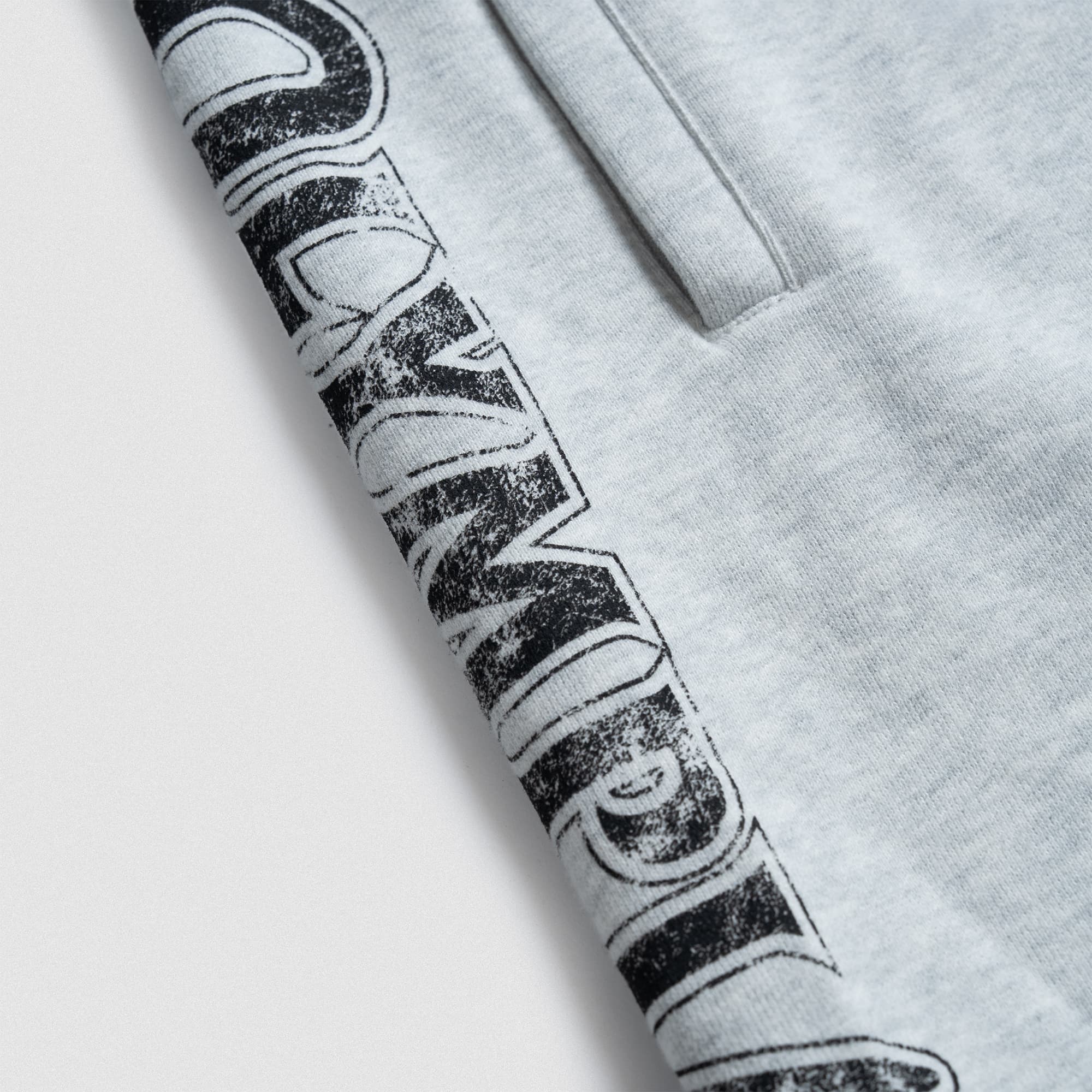Close-up view of the vertical “Olympia” text graphic printed in black with a distressed finish along the leg.