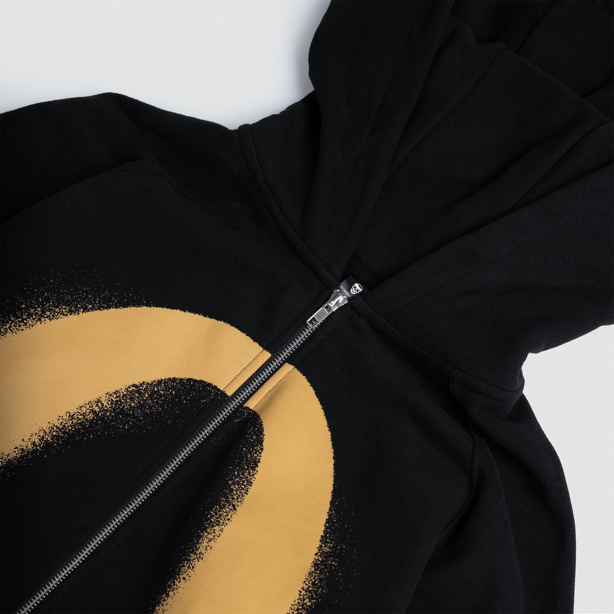 Close-up of the Ring of Fire Zip-Up Hoodie zipper and oversized gold “O” graphic