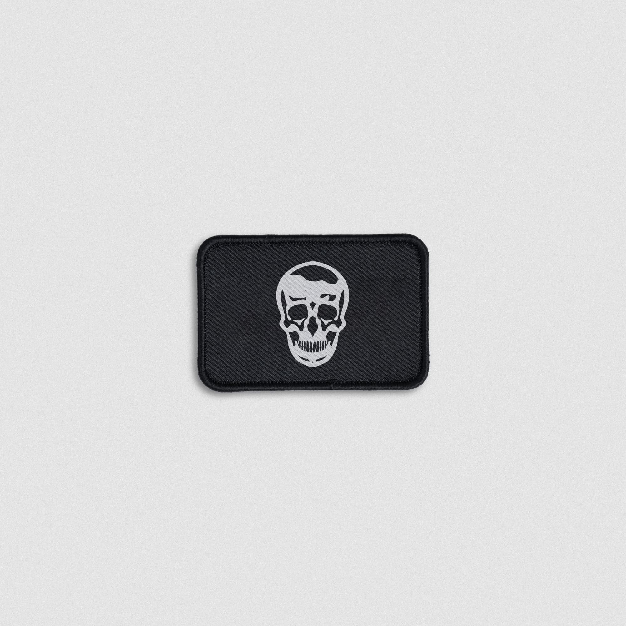 Rectangular black patch featuring a bold white skull graphic with a stitched black border.