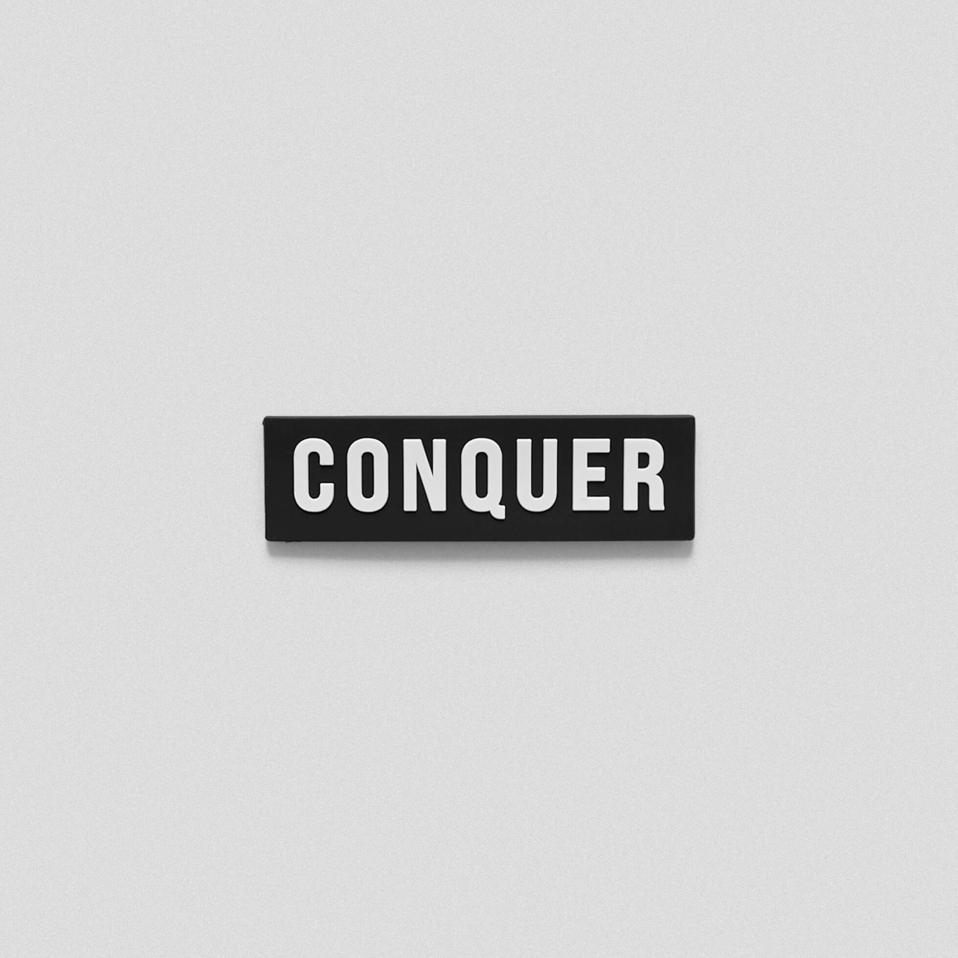 Black white patch that says conquer across.